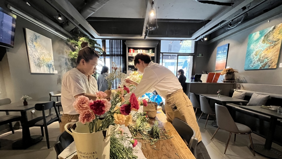 两位聋人咖啡师在打理赠送给客人的鲜花，两边墙上挂着的是聋人林英的画作 谢飞君摄